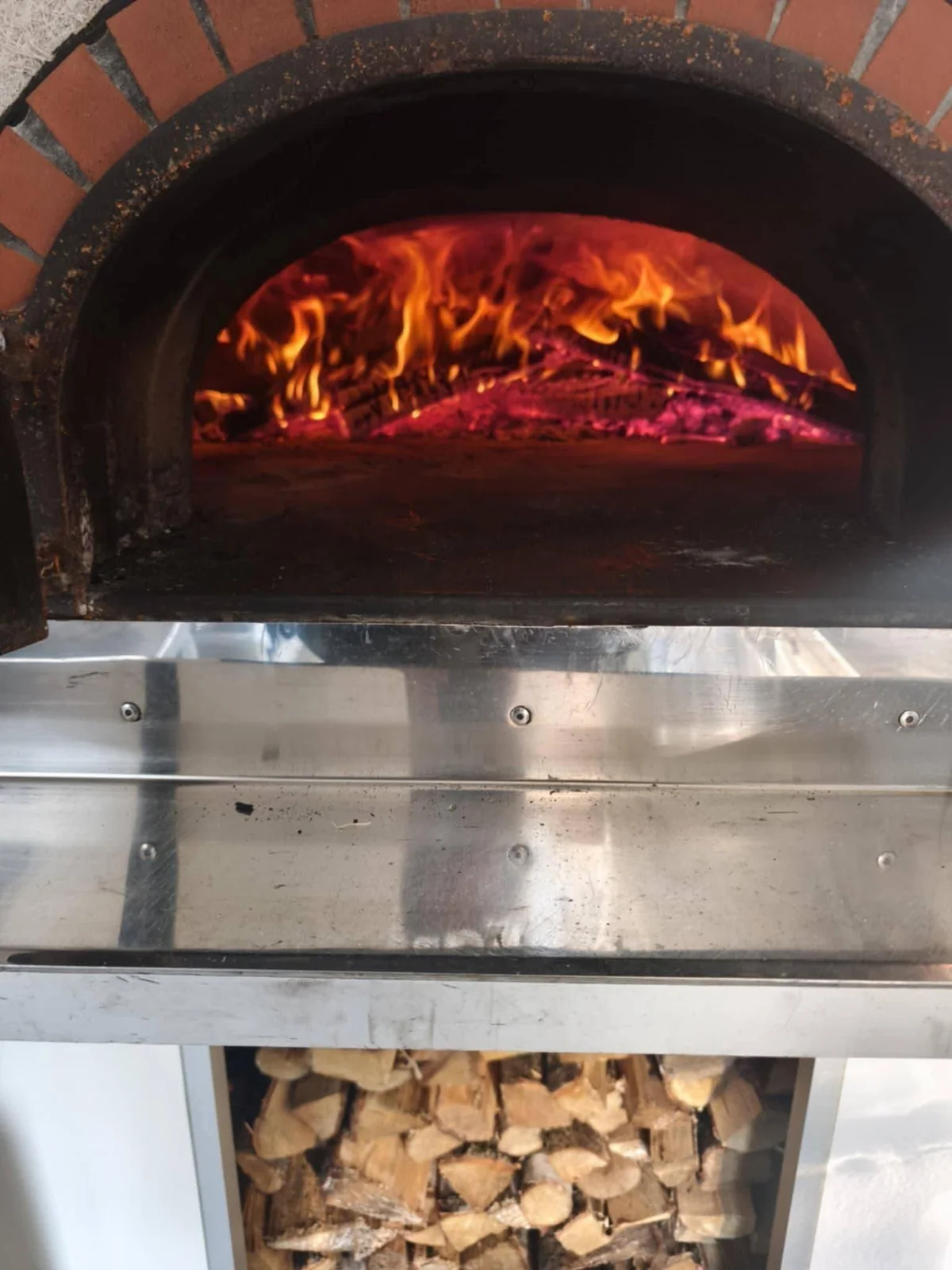 Flammes dans le four à bois en briques de la Pizza Gourmande, bois empilé en dessous